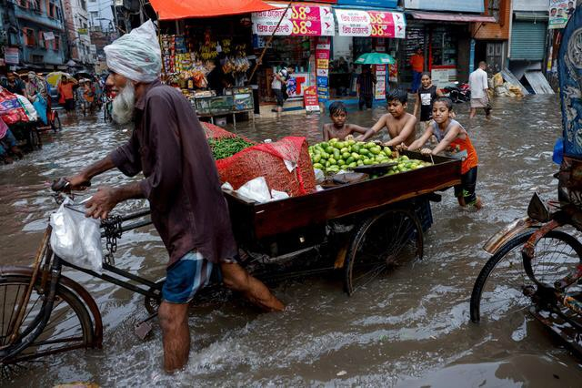 Trẻ em đẩy xe giúp một người bán rau khi đường phố ngập trong mưa lớn ở Dhaka, Bangladesh. (Ảnh: REUTERS/Mohammad Ponir Hossain)