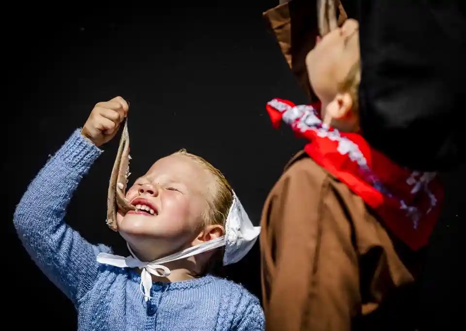 Trẻ em Hà Lan ăn cá trích trong trang phục truyền thống. (Ảnh: Remko de Waal/EPA)