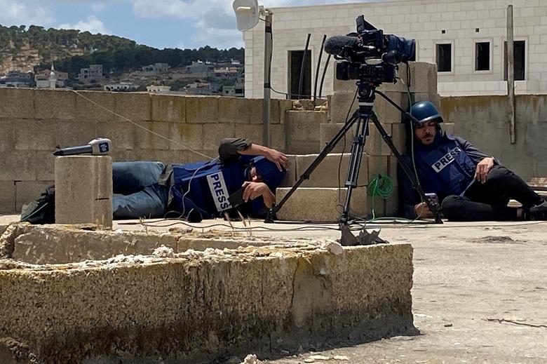 Các nhà báo Palestine tìm chỗ ẩn trong cái nắng thiêu đốt trên mái nhà khi đang đưa tin về một cuộc đột kích của Israel ở Jenin, thuộc Bờ Tây do Israel chiếm đóng. (Ảnh: REUTERS/Ashraf Shaweesh)