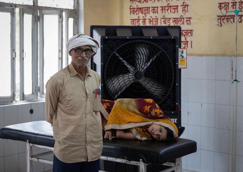 Reshmi Pathak, 30 tuổi, phát bệnh vì nắng nóng, nằm trên cáng khi cha cô đứng cạnh trong phòng cấp cứu tại một bệnh viện ở quận Ballia, bang Uttar Pradesh, Ấn Độ. (Ảnh: REUTERS/Adnan Abidi)