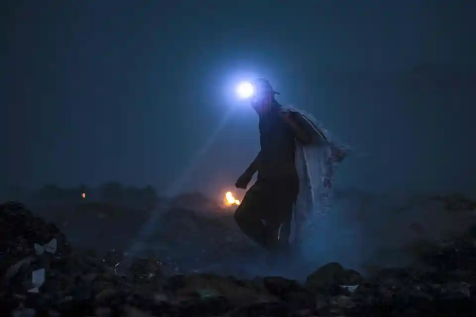 Một người đàn ông rọi đèn pin ở một bãi rác để tìm vật liệu có thể tái chế, hy vọng sẽ bán được để kiếm chút tiền. (Ảnh: Hussein Faleh/AFP/Getty Images)