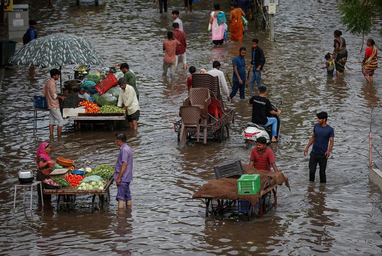 Người dân mua rau từ những người bán hàng rong, những người khác lội qua con đường ngập nước sau mưa lớn ở Ahmedabad (Ấn Độ). (Ảnh: REUTERS/Amit Dave)
