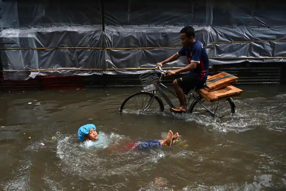 Một đứa trẻ chơi đùa trong dòng nước lũ, trong khi một người khác đạp xe qua sau cơn mưa lớn ở Yangon (Myanmar). (Ảnh: Sai Aung Main/AFP/Getty Images)