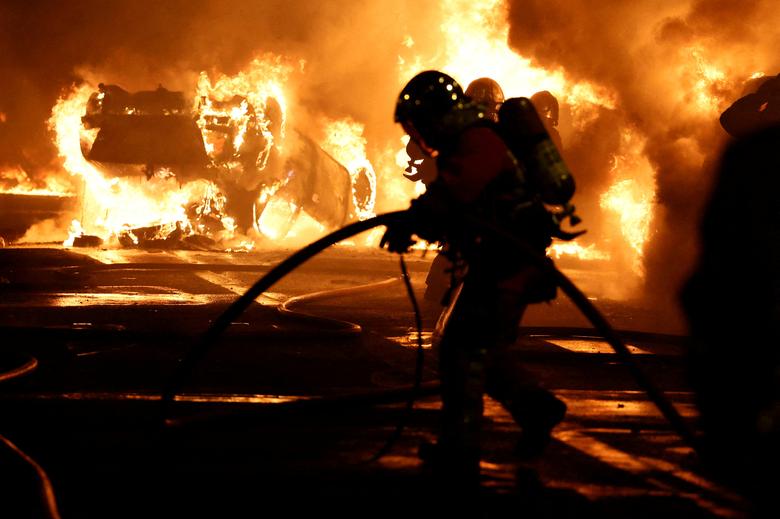 Lính cứu hỏa dập lửa sau khi các phương tiện bốc cháy trong cuộc đụng độ giữa người biểu tình và cảnh sát, sau cái chết của Nahel, một thiếu niên 17 tuổi bị cảnh sát Pháp bắn chết ở Nanterre (ngoại ô Paris, Pháp). (Ảnh: REUTERS/Stephanie Lecocq)