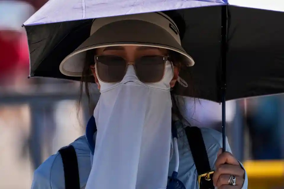 Một người phụ nữ đeo khăn che mặt và che ô khi đi trên đường vào một ngày nắng nóng khắc nghiệt ở Bắc Kinh (Trung Quốc). (Ảnh: Andy Wong/AP)