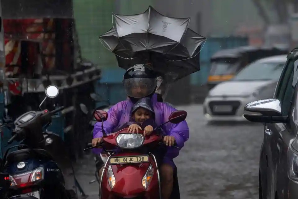 Một người đi xe máy cùng một bé trai vượt qua cơn mưa lớn ở Mumbai (Ấn Độ). (Ảnh: Rafiq Maqbool/AP)