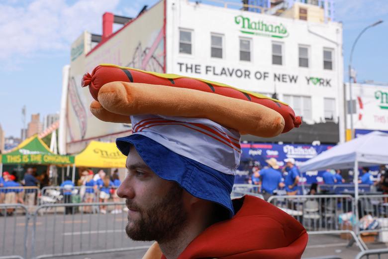 Một người đàn ông đội chiếc mũ có hình xúc xích trước thềm Cuộc thi ăn xúc xích quốc tế nổi tiếng lần thứ tư tại Đảo Coney ở Thành phố New York (Hoa Kỳ). (Ảnh: REUTERS/Amr Alfiky)