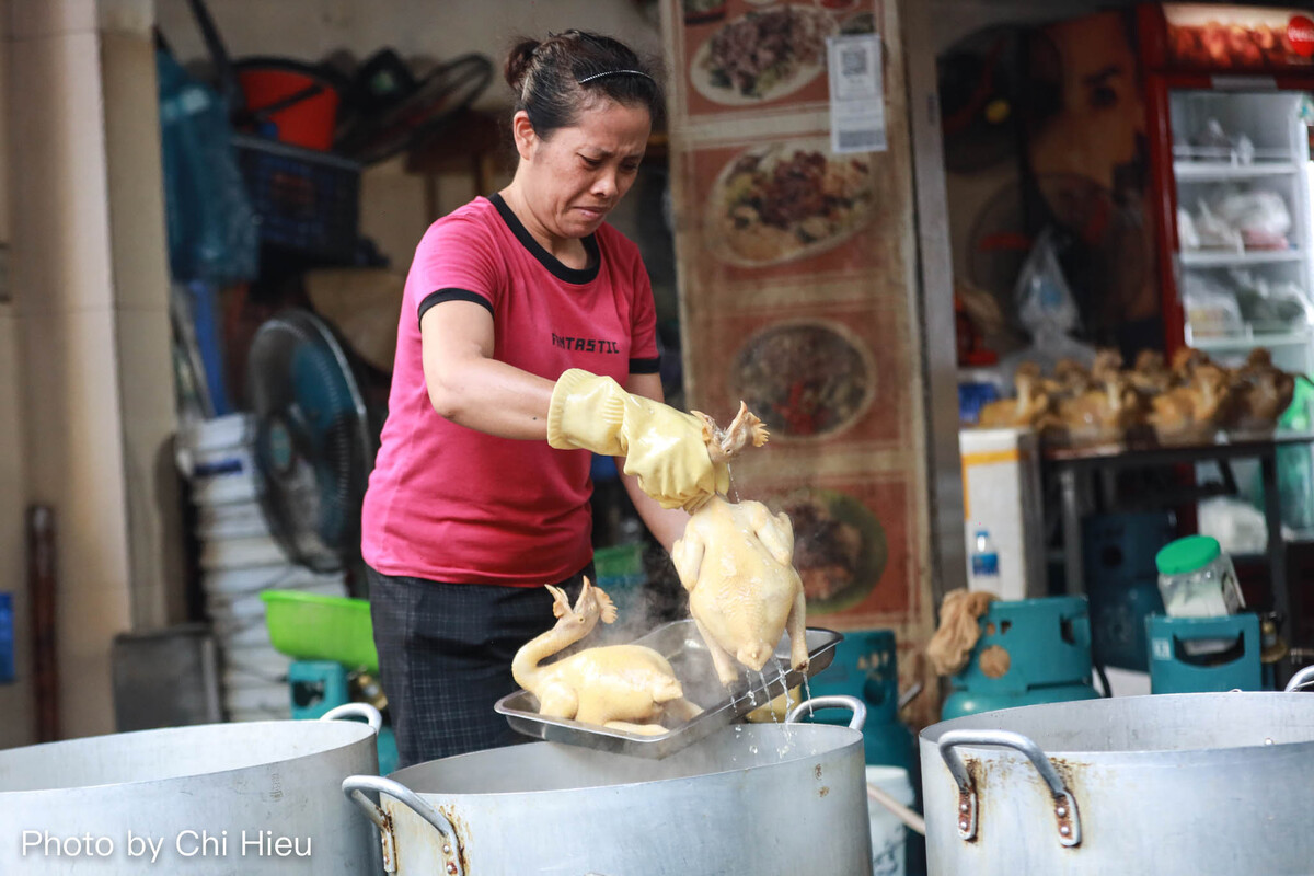 Số lượng khách quá đông khiến, một người phụ nữ chế biến gà chỉ đeo chiếc găng tay mỏng để lấy gà từ nồi nước luộc nóng hổi.