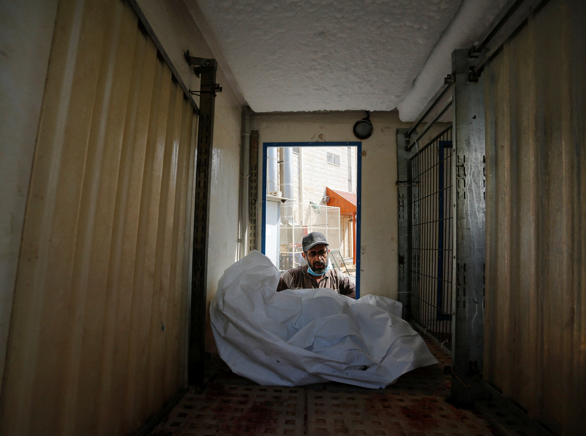 Công nhân đẩy thi thể của một người Palestine thiệt mạng trong cuộc không kích vào bên trong xe tải. (Ảnh: REUTERS)