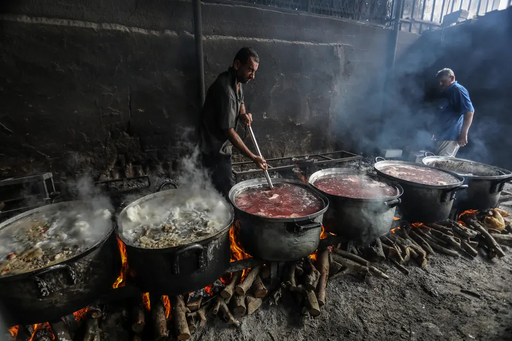 Tình nguyện viên Palestine chuẩn bị bữa ăn cho các gia đình phải di dời từ phía Bắc và trung tâm thành phố về phía Nam do các cuộc tấn công của Israel vào Dải Gaza. (Ảnh: Anadolu Agency/Getty Images)