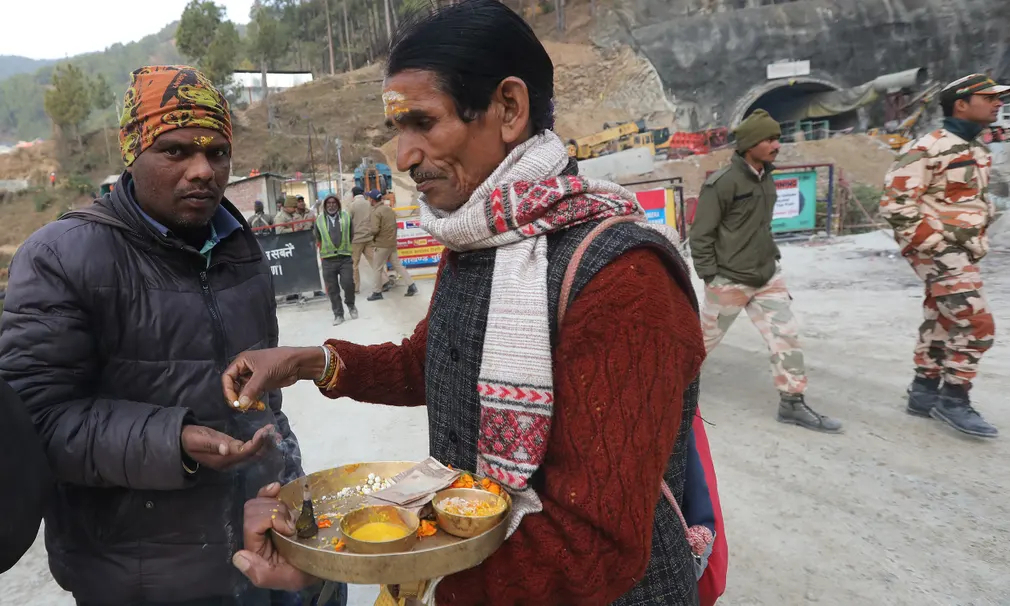 Linh mục Hindu phân phát lễ vật cho một công nhân đến đường hầm Silkyara (Uttarkashi, Ấn Độ) bị sập khi đang được xây dựng để tham gia hoạt động cứu hộ. (Ảnh: Harish Tyagi/EPA)