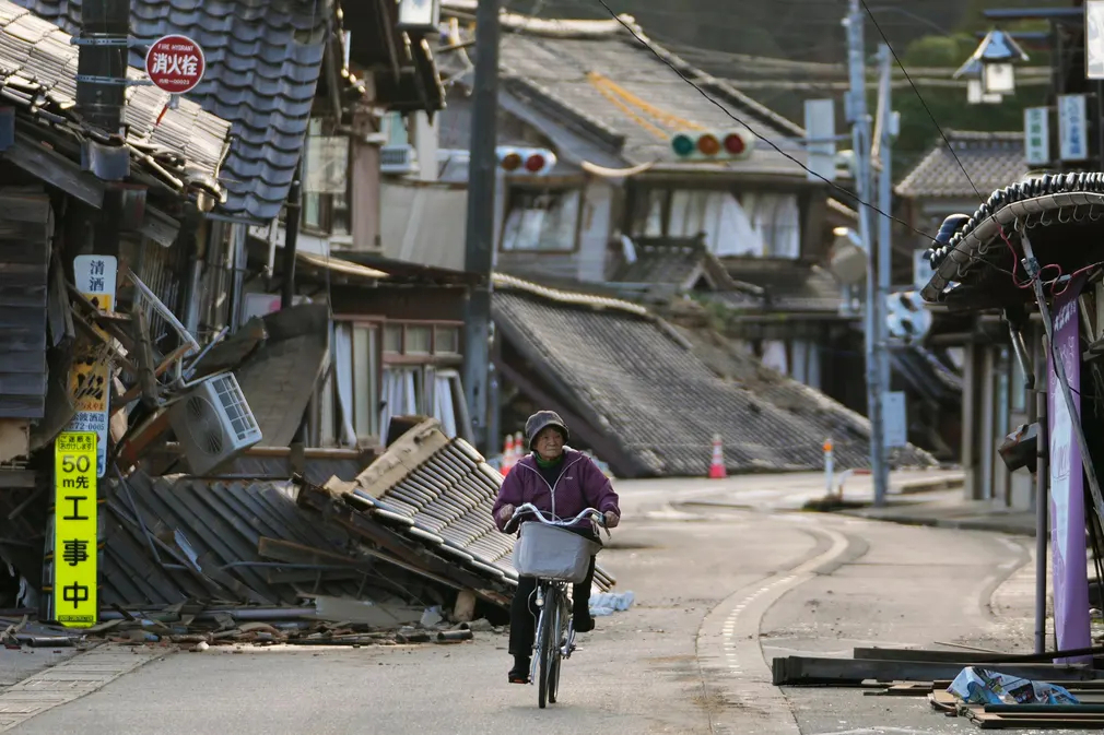 Người phụ nữ đạp xe dọc con phố vắng vẻ qua những tòa nhà bị phá hủy trong trận động đất hôm 1/1 ở Nhật Bản. (Ảnh: Hiro Komae/AP)