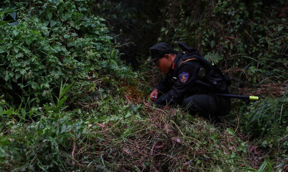 Một chiến sĩ cảnh sát cơ động đang dùng bật lửa đốt bụi cỏ ven rừng để chống muỗi.