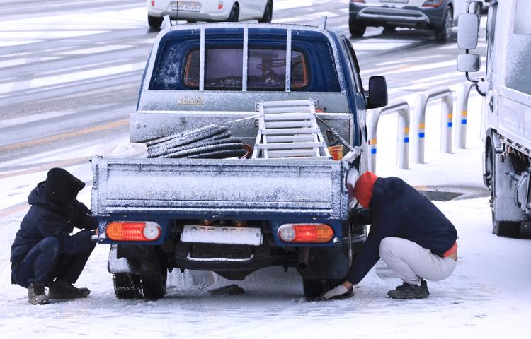 Một tài xế xe tải buộc dây xích tuyết vào lốp xe ô tô ở Jeju khi đợt lạnh tràn vào đảo. (Ảnh: Yonhap)    