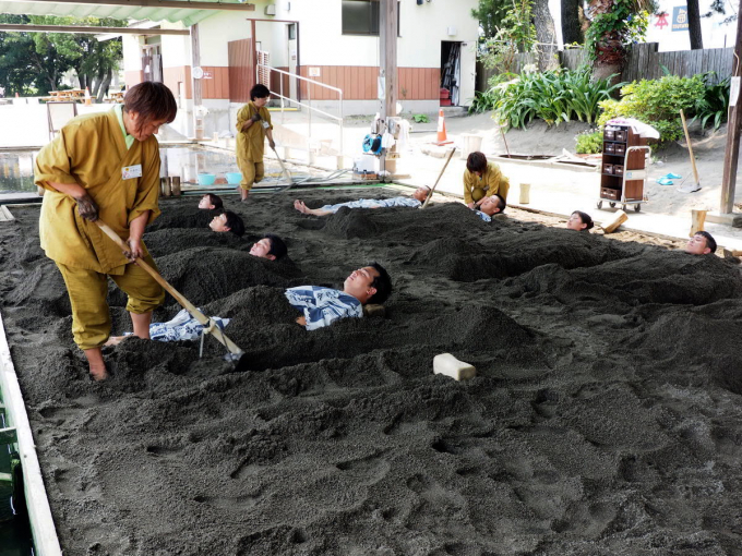 Nhân viên dùng xẻng để xúc cát đắp lên cho du khách