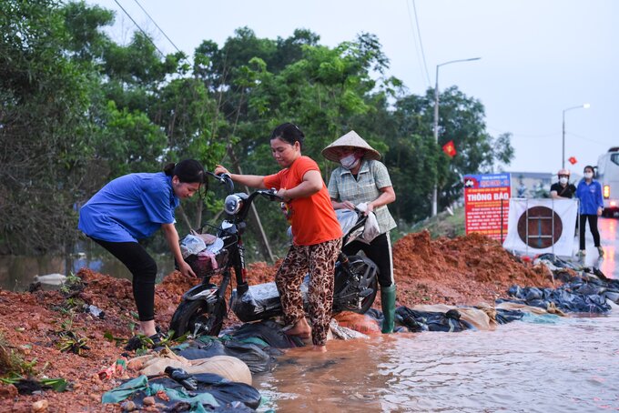 Một số người dân di chuyển bằng xe đạp điện phải nhờ đến sự trợ giúp của thanh niên tình nguyện và những người xung quanh mới đi được qua đoạn ngập nước sâu.