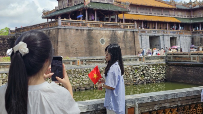 Một nữ du khách trẻ với lá cờ Tổ quốc trên tay đứng chụp hình trước cổng Ngọ Môn.