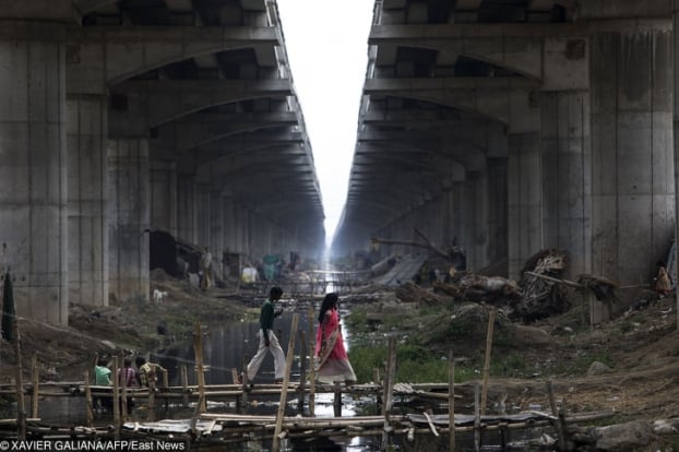   Người dân đi bộ qua cây cầu trên con kênh bẩn ở Danapur, Ấn Độ. Bên cạnh đó là trẻ em đang chơi đùa  