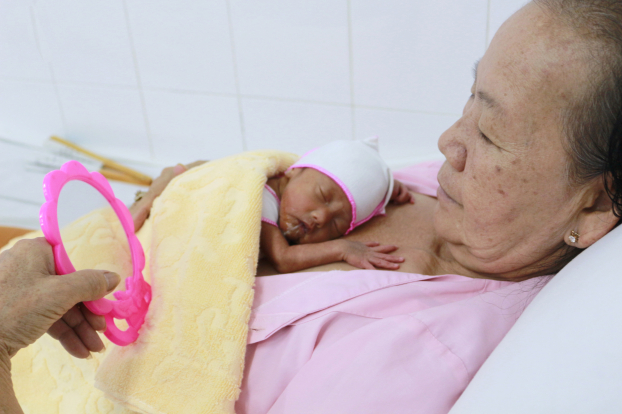   Một trong ba em bé sinh ba non tháng đang được bà ủ ấm  