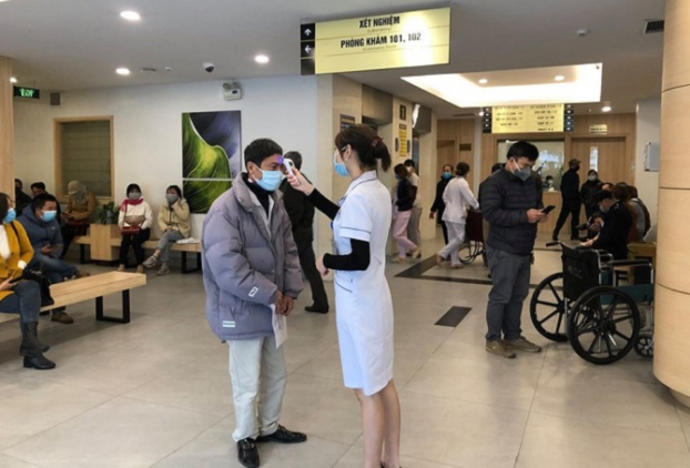   Nhân viên y tế của Bệnh viện Ung bướu Hà Nội đo thân nhiệt cho bệnh nhân trước khi vào khám bệnh  