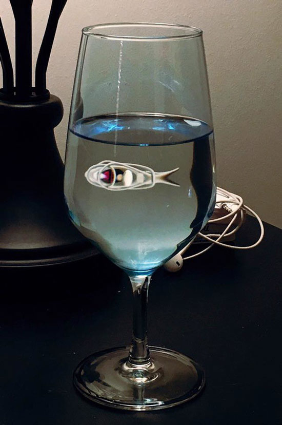   Hình phản chiếu của chiếc tai nghe trên ly nước trông giống như có một con cá trắng đang bơi trong ly  