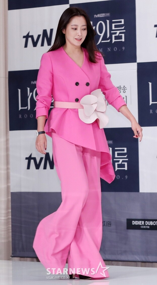 Kim Hee Sun mặc suit hồng với quần ống loe, thắt lưng hoa nhấn eo và áo có thiết kế xòe rộng ở hông giúp tạo đường cong