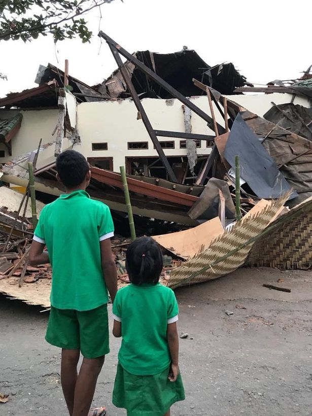 Hai đứa trẻ mặc đồng phục của Mái ấm Peduli Anak đứng thất thần nhìn ngôi nhà bị phá hủy do động đất - Ảnh: Pedulianak/Twitter.