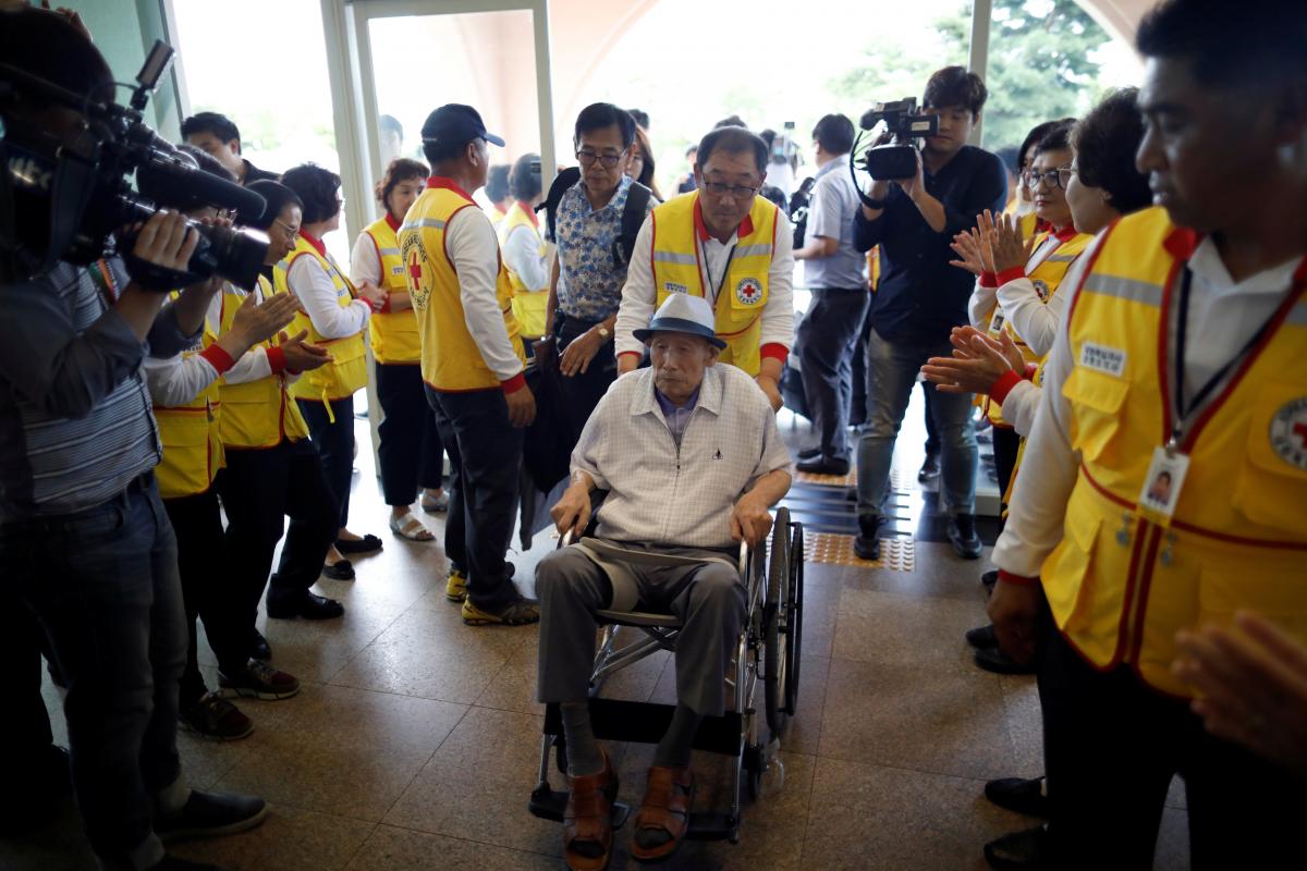 Một người đàn ông được chọn nhưng phải ngồi xe lăn đi dến khách sạn tại Sokcho - Ảnh: Reuters.