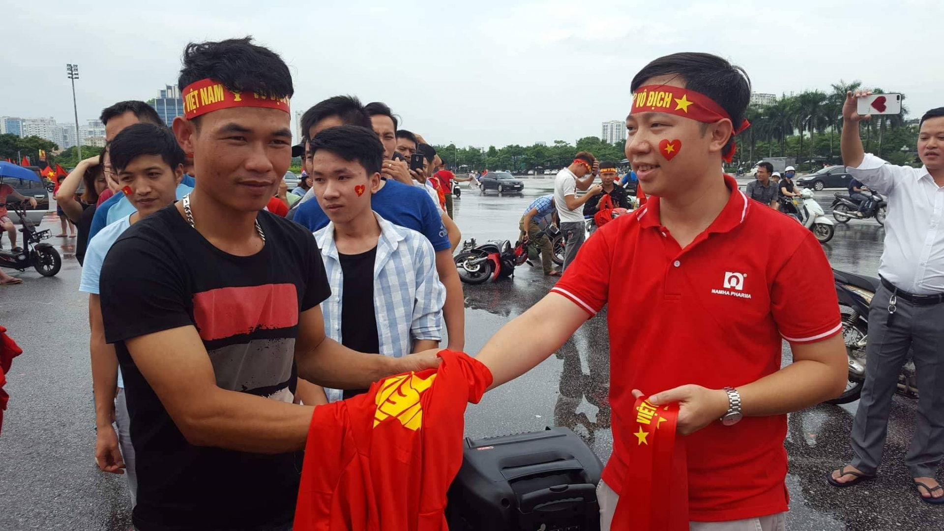 Mặc dù trời mưa khá nặng hạt nhưng tại khu vực trước sân vận động Mỹ Đình, nhiều người hâm mộ vẫn xếp hàng nhận áo tặng cổ vũ đội tuyển Việt Nam của Cty dược phẩm Nam Hà