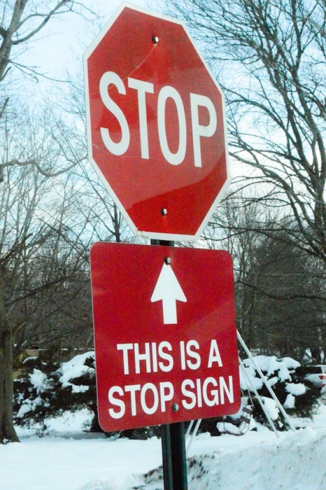 Bên dưới tấm biển 'Dừng lại' là một tấm biển chỉ lên trên viết rằng: 'Đây là một tấm biển báo dừng lại'