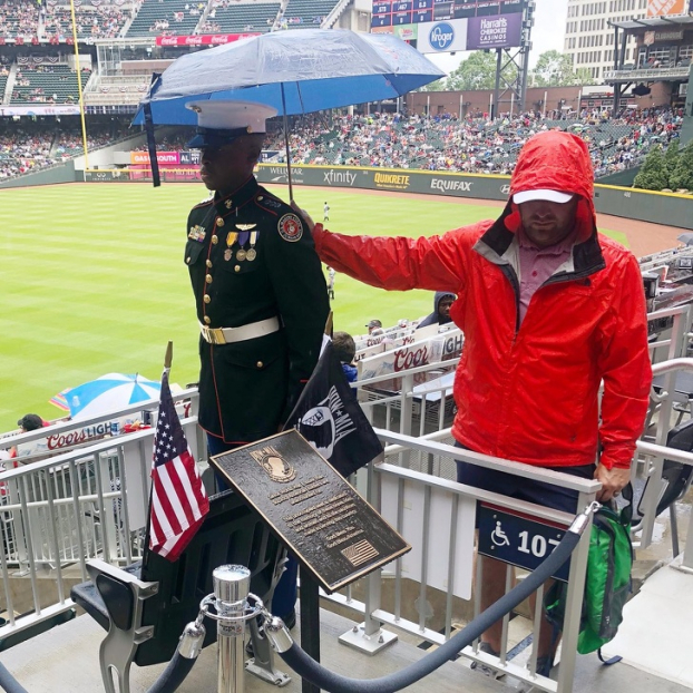   Một fan hâm mộ bóng chày đang cầm một chiếc ô che cho một thành viên của JROTC (Đội Huấn luyện Thiếu sinh quân Dự bị) trong Ngày Tưởng niệm Liệt sĩ của Mỹ  