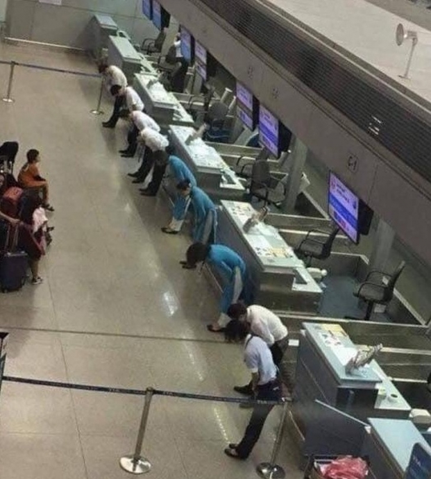   Các nhân viên sân bay cúi đầu xin lỗi khách hàng vì trễ chuyến bay  
