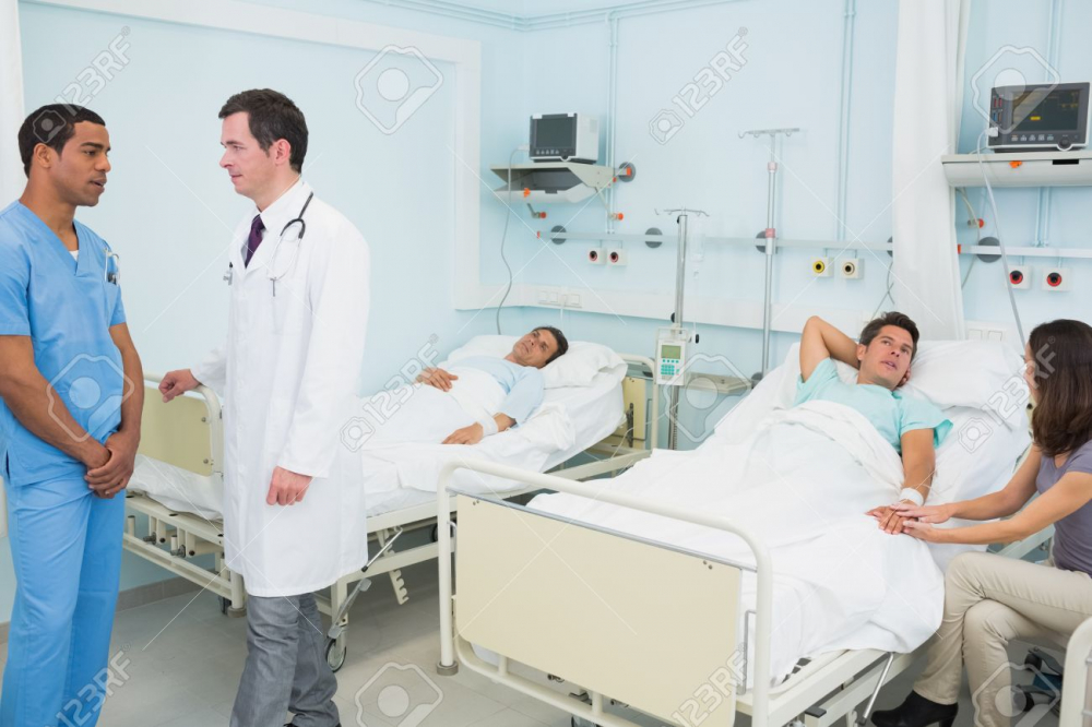 18095412-Doctor-and-male-nurse-in-a-hospital-room-with-patient-resting-Stock-Photo