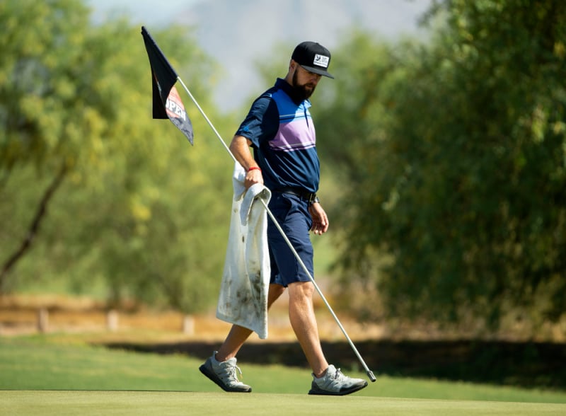 Charlie Beau, caddy cho tay golf PGA Tour Kevin Streelman, cầm cây cờ với một chiếc khăn trên green thứ 18. Ảnh: Rob Schumacher/USA TODAY Sports.