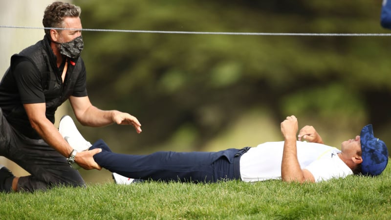 Brooks Koepka có ba lần phải nằm trên cỏ để HLV Marc Wahl kéo chân và giúp giãn phần cơ hông trái (Ảnh: Getty Images)