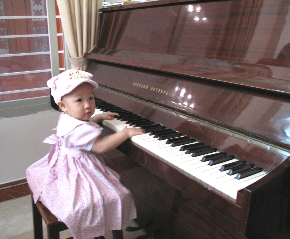 Bé Dương Cầm Nga, cháu nội bà Cần, bên cây đàn dương cầm Tháng Mười Đỏ của Nga. Ảnh: Gia đình cung cấp.