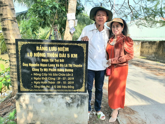 Ông Nguyễn Ngọc Lang và vợ là bà Lê Thị Truyền chụp hình tại bảng lưu niệm công trình lộ nông thôn dài 5km do ông Lang tài trợ.
