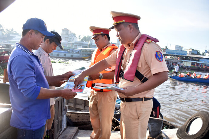Lực lượng Phòng PC08B Công an TP Cần Thơ phát tờ rơi tuyên truyền quy định của Luật Giao thông đường thủy nội địa cho tiểu thương neo đậu tại chợ nổi Cái Răng.