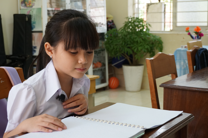 Bé Nguyễn Ngọc Phương Linh khiếm thị, học lớp 4 đang tập đọc trên sách chữ nổi