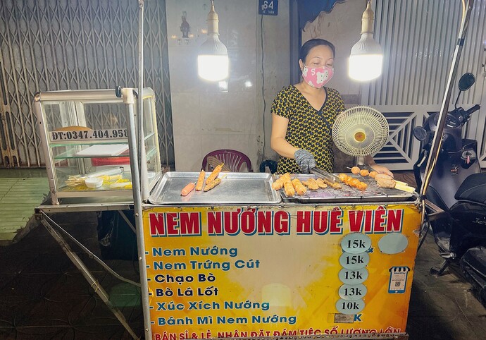 Nằm giữa con phố ẩm thực Hồ Xáng Thổi (Số 64 Đề Thám, phường Tân An), xe nem nướng cô Hoa vẫn luôn đắt khách vào những buổi chiều tan tầm hơn 7 năm nay. Độ 2 giờ chiều, bếp than đã nghi ngút khói, đến tầm 8 giờ tối, đồ ăn trên vĩ gần như đã hết sạch sẽ.