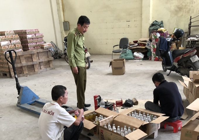 Lực lượng chức năng phát hiện 2 lao động đang tẩy xóa ngày sản xuất, hạn sử dụng trên nắp chai. Ảnh: Đội QLTT Hà Nội cung cấp.