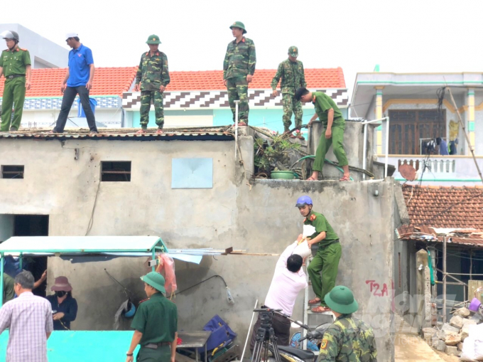 Những người lính giúp dân đưa những bao cát lên cao giằng mái nhà để tôn khỏi bay trong bão. Ảnh: Vũ Đình Thung.
