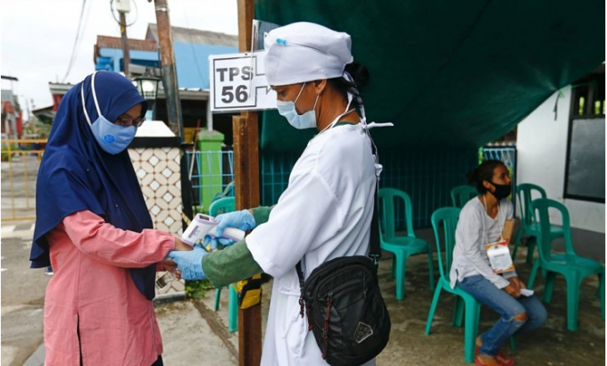 Một cử tri đeo khẩu trang y tế được đo thân nhiệt trước điểm bầu cử khu vực ở Depok, ngoại ô Jakarta ngày 9 tháng 12 năm 2020. Ảnh: Reuters