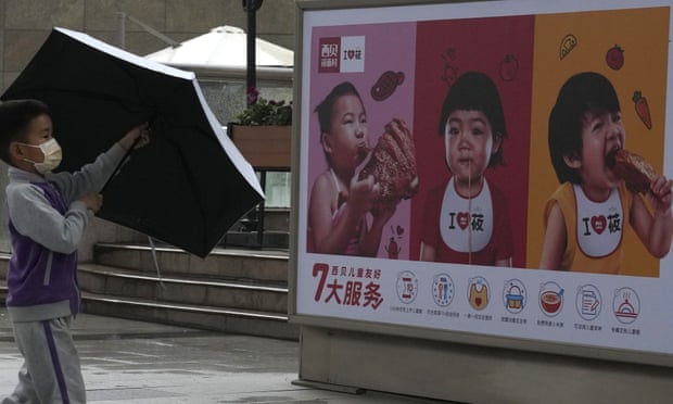 Hình ảnh một đứa trẻ đi ngang qua áp phích quảng cáo của một nhà hàng kinh doanh đồ ăn nhanh ở thủ đô Bắc Kinh hôm 31/5/2021, ngày Bộ Chính trị thông báo 'chính sách ba con' để tăng tỷ lệ sinh. Ảnh: AP