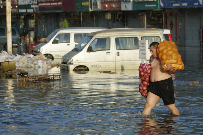 A man carries bags of onions on a flooded street in Xinxiang in central China's Henan Province Monday, July 26, 2021. A United Nation-backed panel plans to release a highly anticipated scientific report on Monday, April 4, 2022, on international efforts to curb climate change before global temperatures reach dangerous levels. Photo: AP