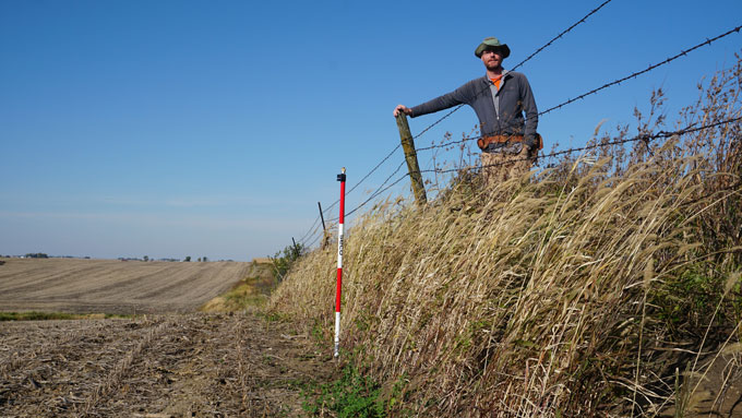 Geologist Isaac Larsen stands at an erosional escarpment, a meeting point of farmland and prairie, in Stinson Prairie, Iowa. Studying these escarpments shows there’s been a startling amount of erosion in the U.S. Midwest since farming started there more than 150 years ago. Photo: sciencenews