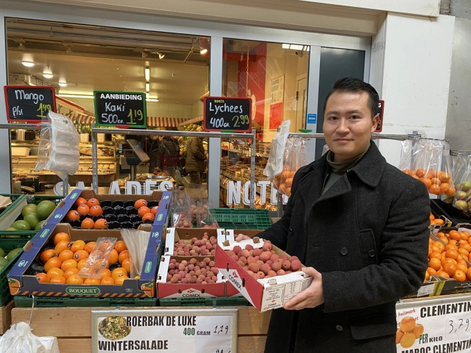 Mr. Nhu Nguyen next to a shelf selling lychee in the Dutch market.