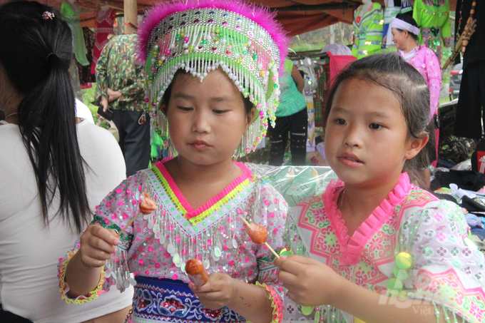 Những đứa trẻ ở Bản Tèn vừa ngồi xem người lớn thi múa hát, vừa ăn xúc xích (món ăn mà ở vùng cao không có). Ảnh: Nguyễn Hoàn.