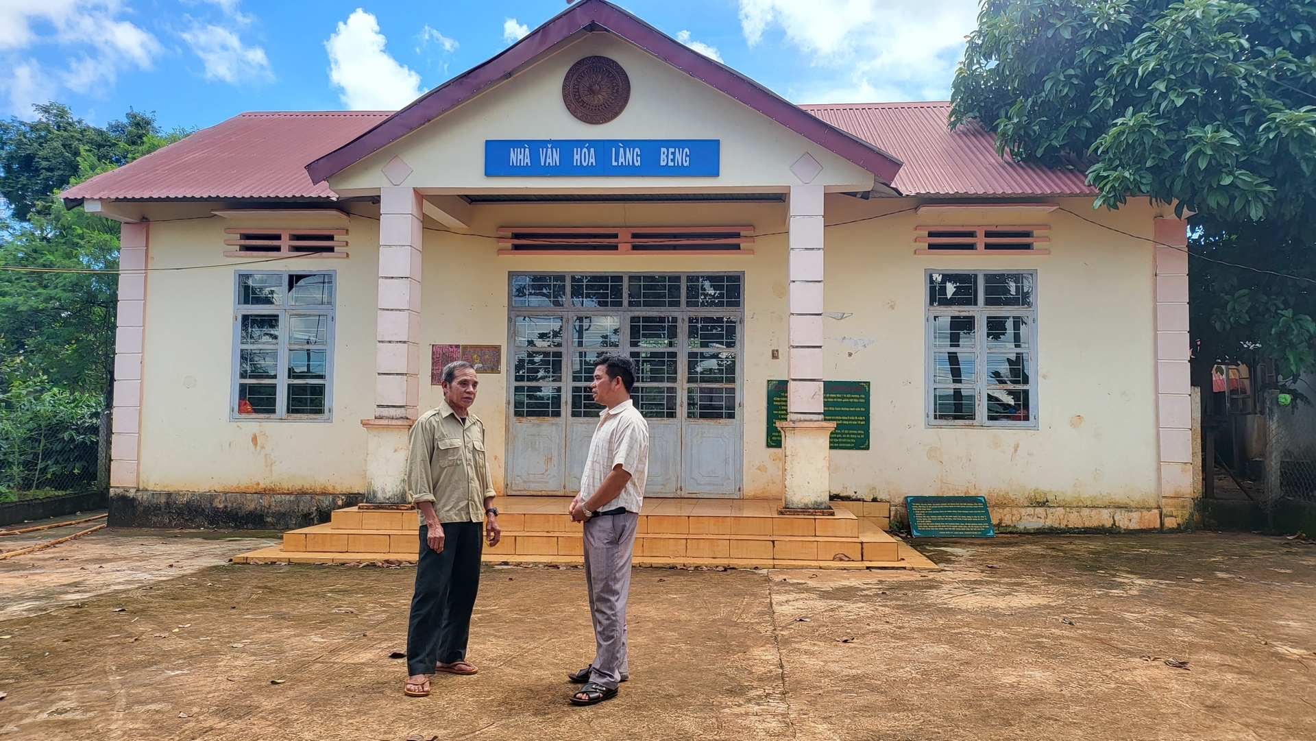 Già Rơ Châm Chích (bía trái) bên cạnh nhà văn hoá làng Beng. Già đã hiến đất cho làng xây nhà văn hóa. Ảnh: Tuấn Anh. 