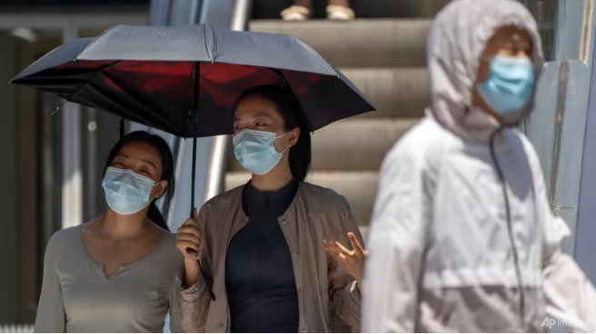 People carry umbrellas and wear long clothing to protect themselves from the sun as they walk at a shopping and office complex on an unseasonably hot day in Beijing, Jun 7, 2023.  Photo: AP/Mark Schiefelbein